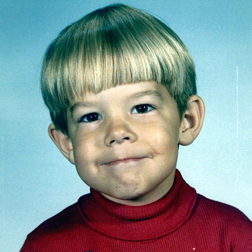 A young boy wearing a red turtle neck sweater.