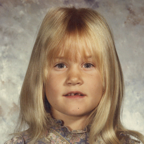 A little girl with blond hair is posing for a picture.
